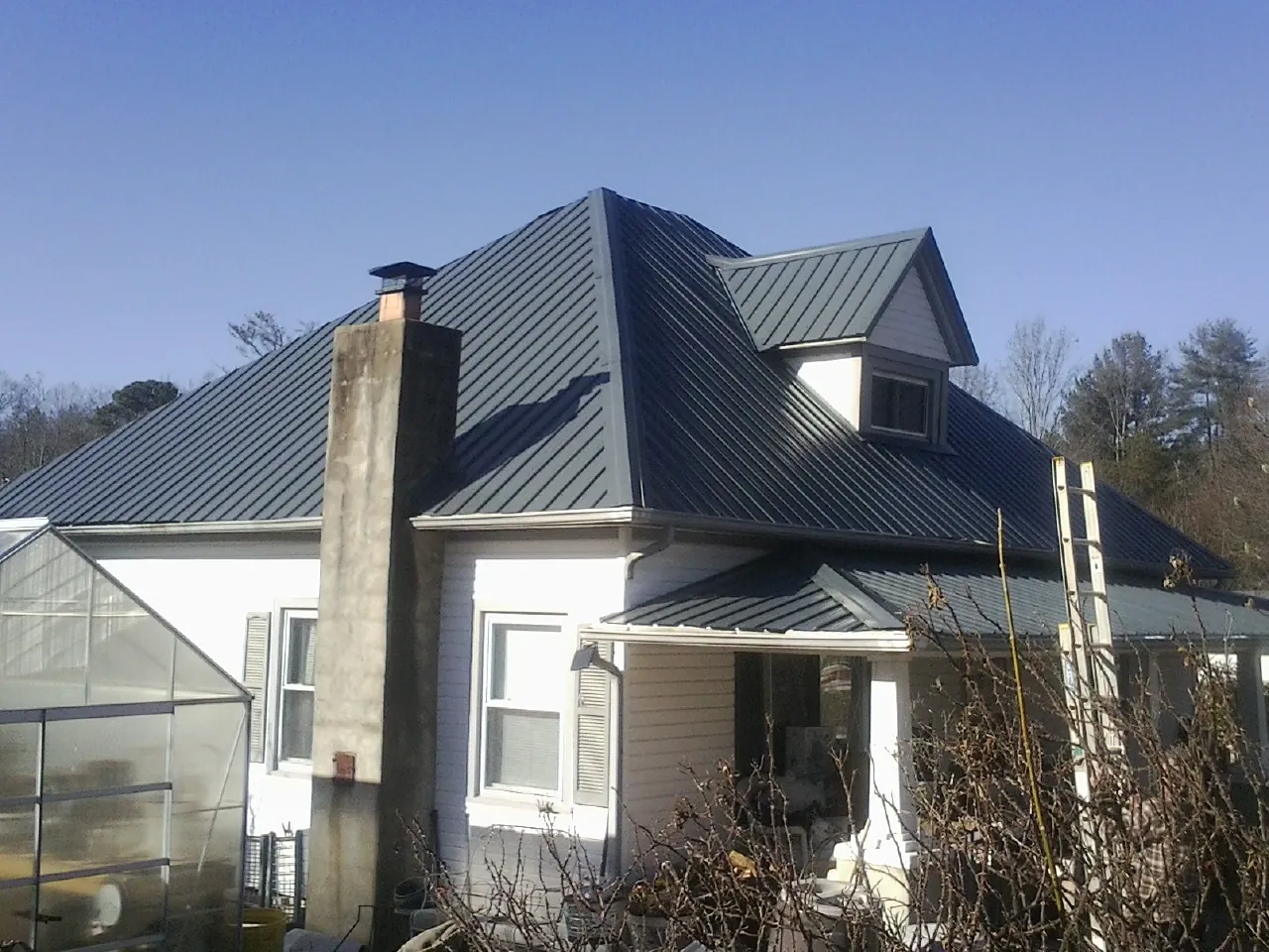 Dark blue standing seam metal roof on a white farmhouse with dormer — Slate & Tile Roof Repair by Roofing Brothers in Point Harbor