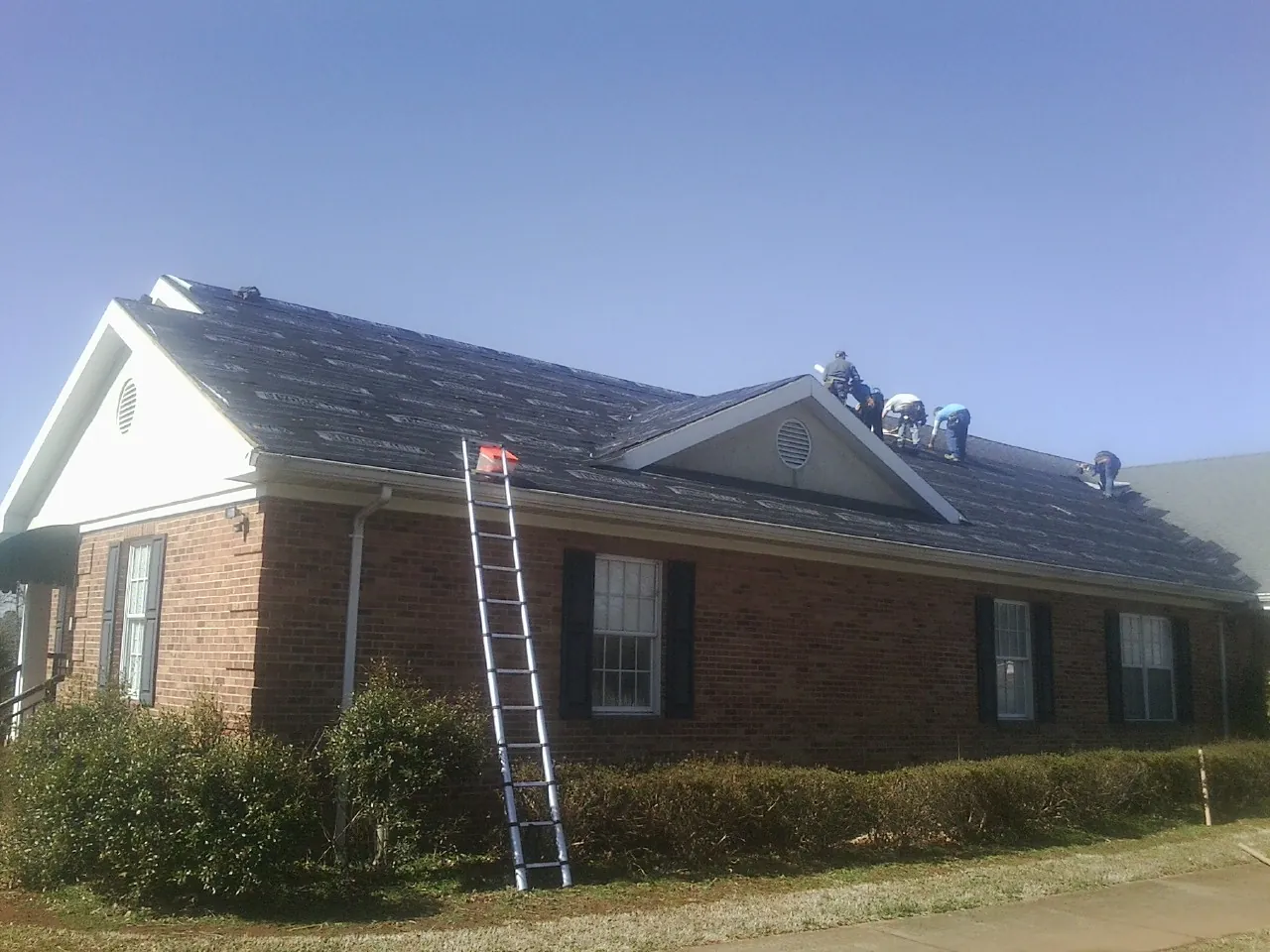 Crew tearing shingles off a brick ranch roof with a ladder set — Metal Roof Repair work by our crew in Point Harbor