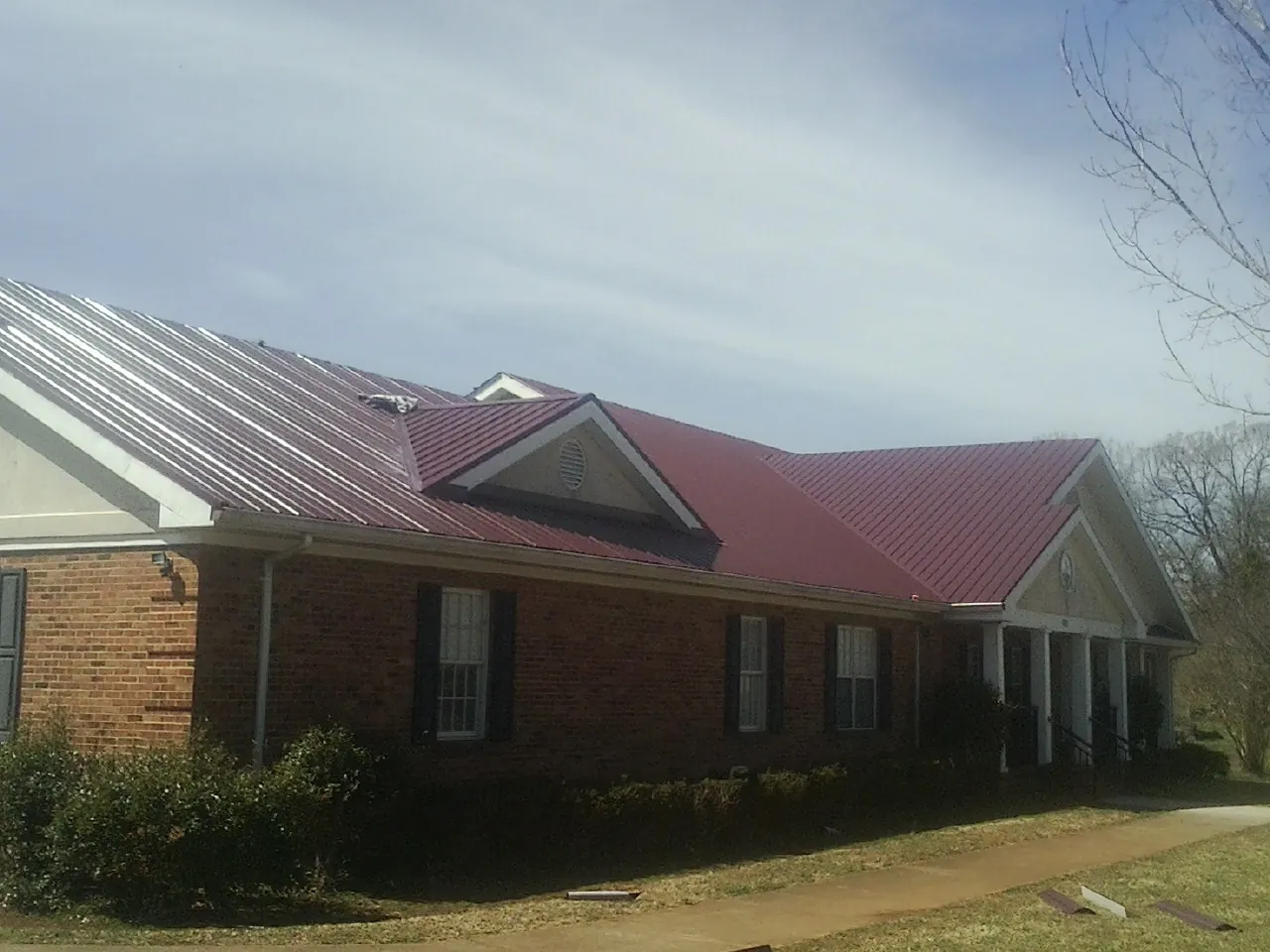 Red metal roof with gabled entries on a long brick building, from a Hail Damage Roof Repair job in Point Harbor