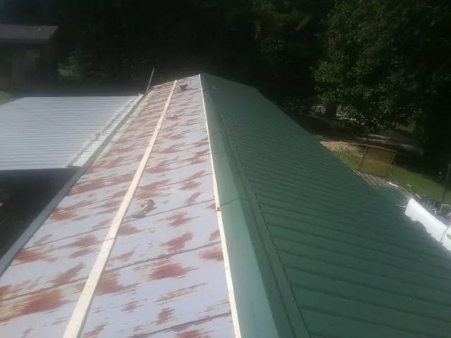 Old rusted panels beside newly installed green metal roofing — Wind Damage Roof Repair by Roofing Brothers in Point Harbor