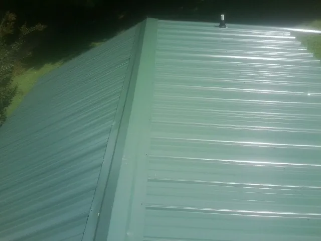 New green metal panels meeting at the ridge of a roof — Flat Roof Repair work by our crew in Point Harbor
