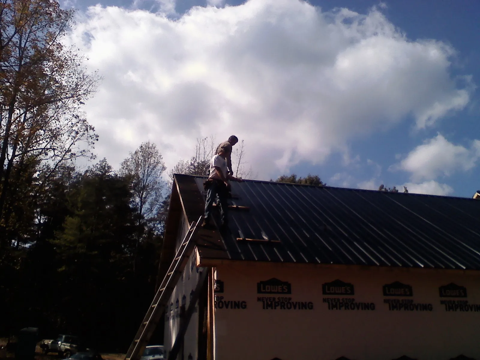 Roofer fastening dark metal panels high against a cloudy sky, from a Roof Inspection job in Point Harbor