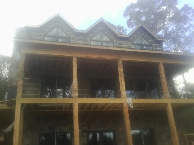 Dormers and porch framing on a large log home under construction — Roof Coating work by our crew in Point Harbor