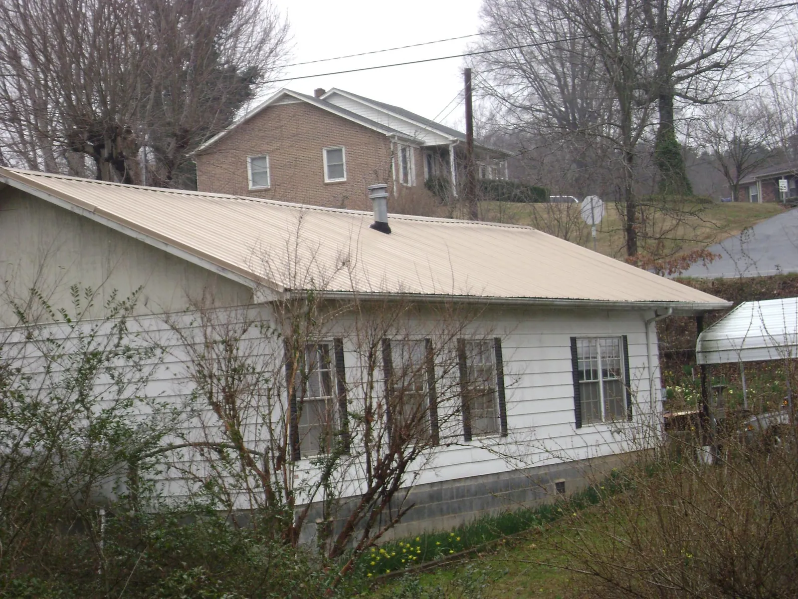 Tan metal roof on a white sided house set into a hillside — Commercial Roofing by Roofing Brothers in Point Harbor